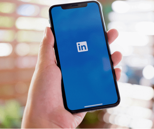 Hand holding a smartphone displaying the LinkedIn app logo on the screen