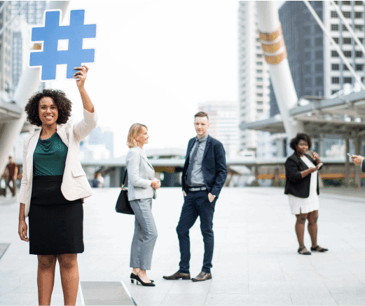Woman holding a hashtag symbol while three business professionals stand and talk outdoors